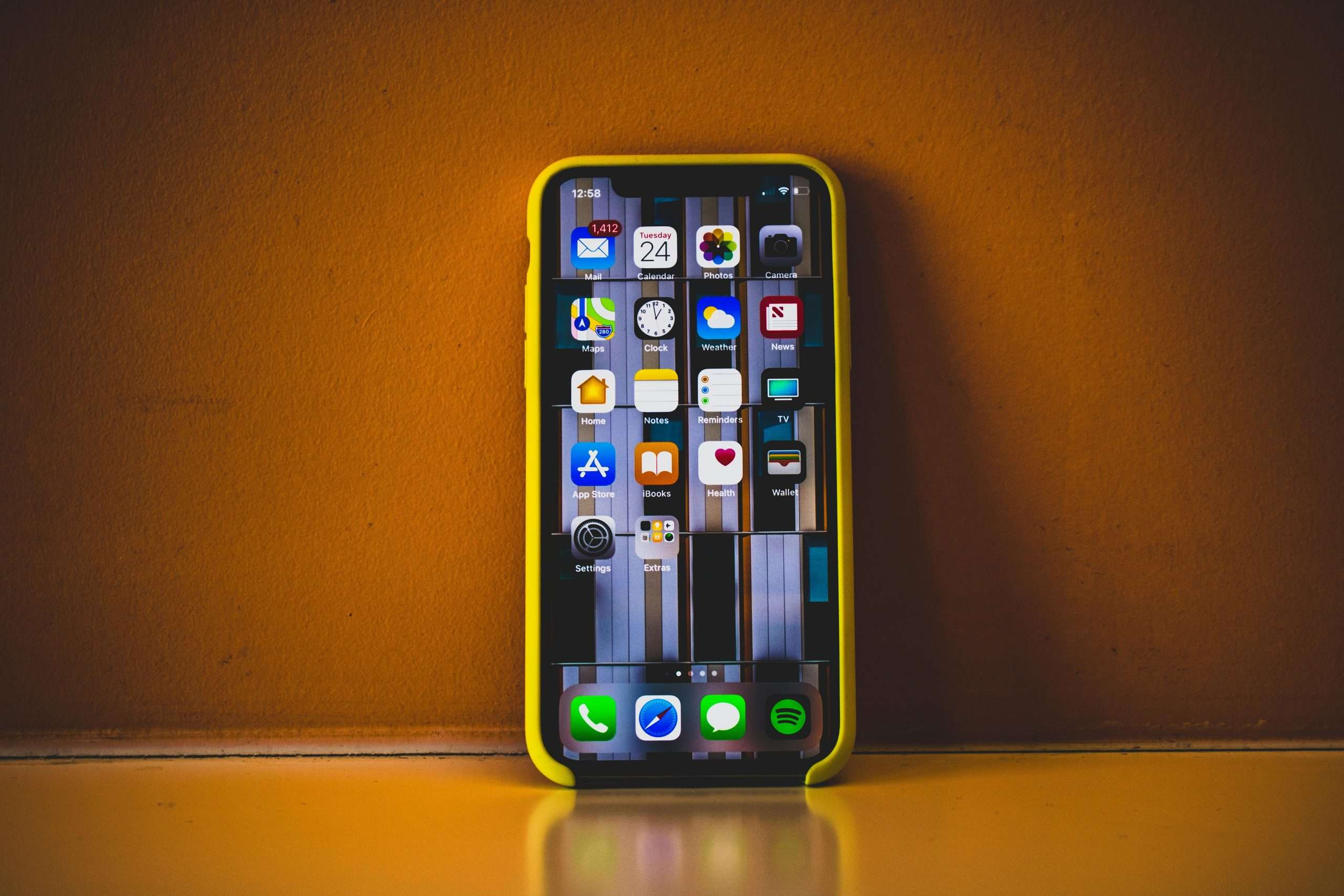 Close-up of a smartphone with a yellow case displaying various app icons, reflecting on a surface.