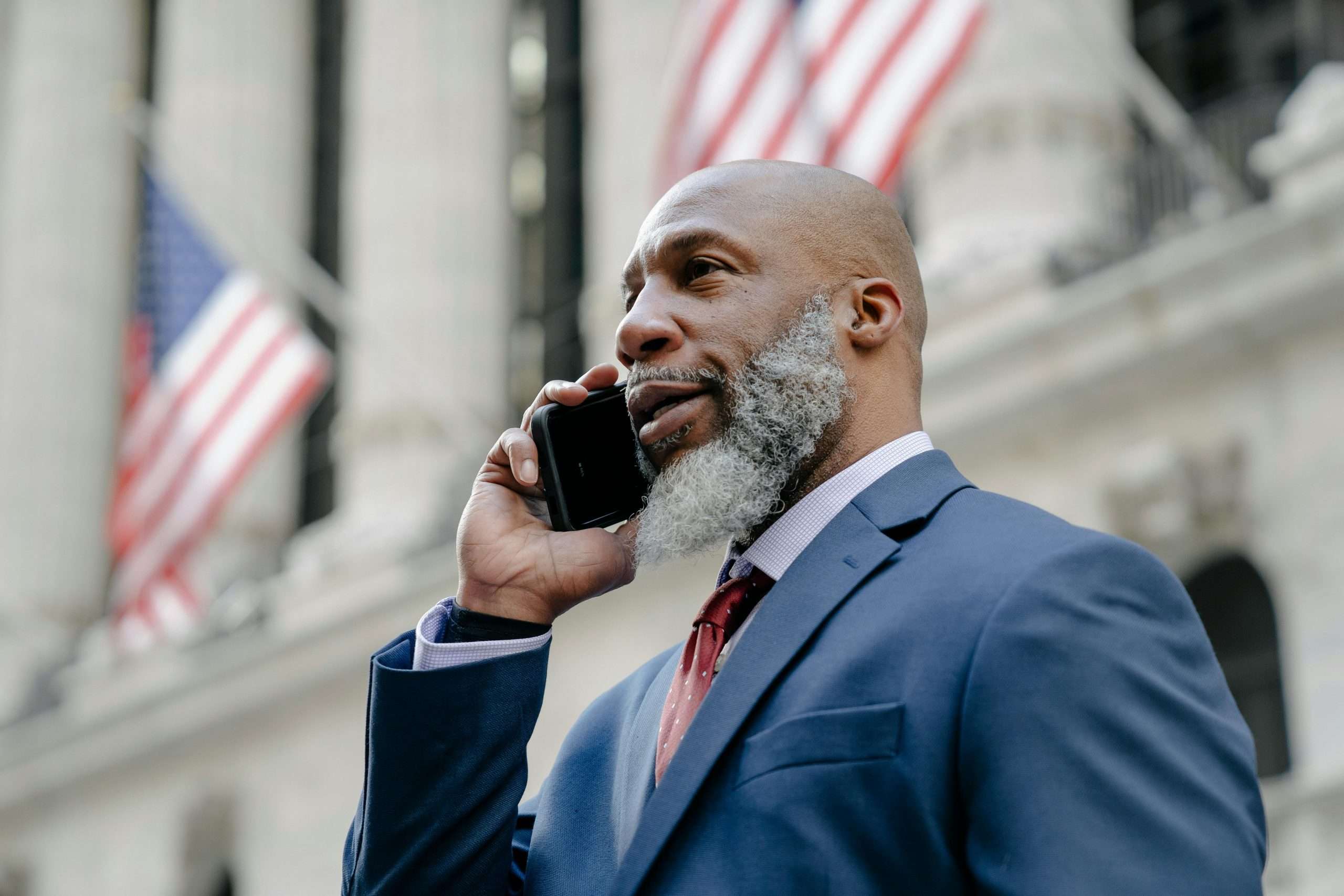 Confident businessman in a suit talking on phone with American flags in the background.