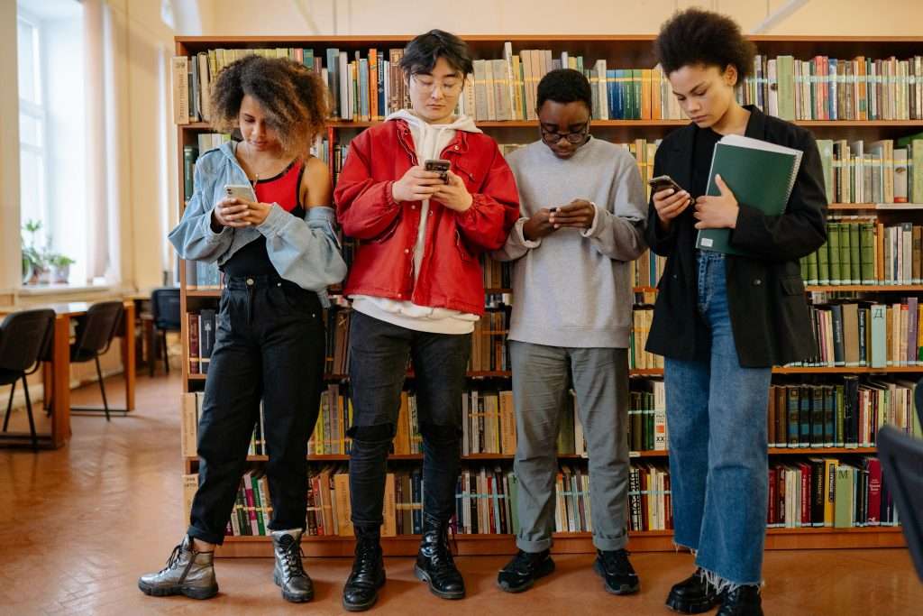 A group of university students using smartphones while standing in a library.